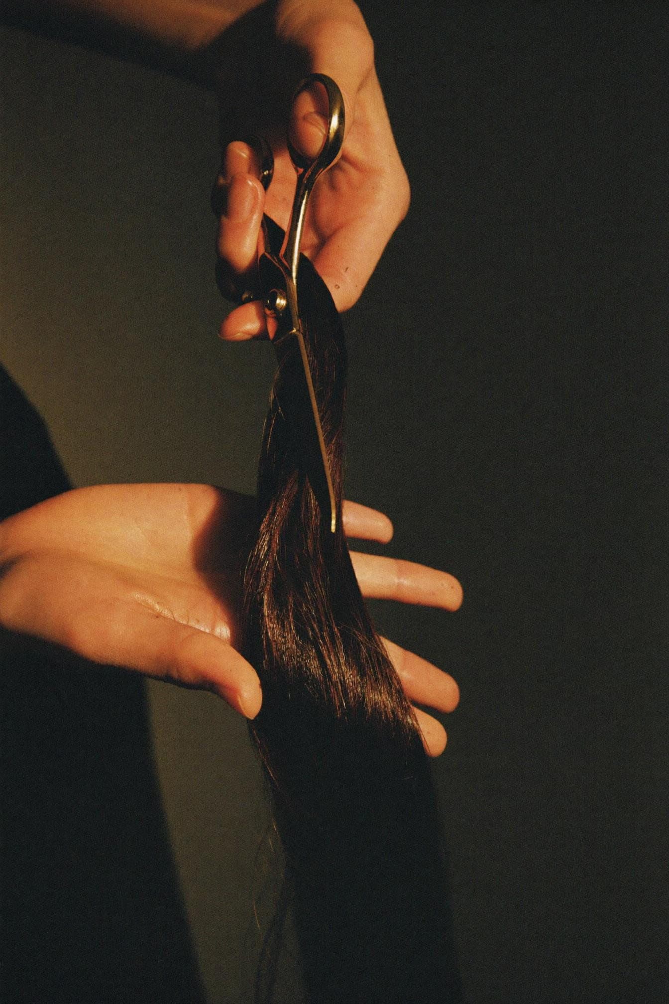 Stylist's hands with gold scissors and a strand of glossy hair, in warm light